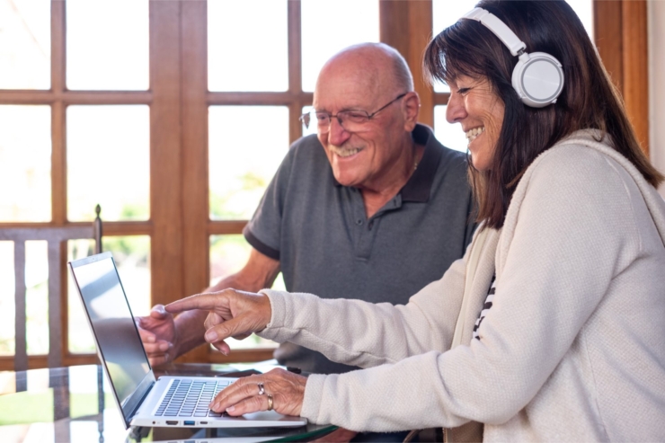 Sharing a joyful moment, two residents engage with a laptop in a bright, inviting space.