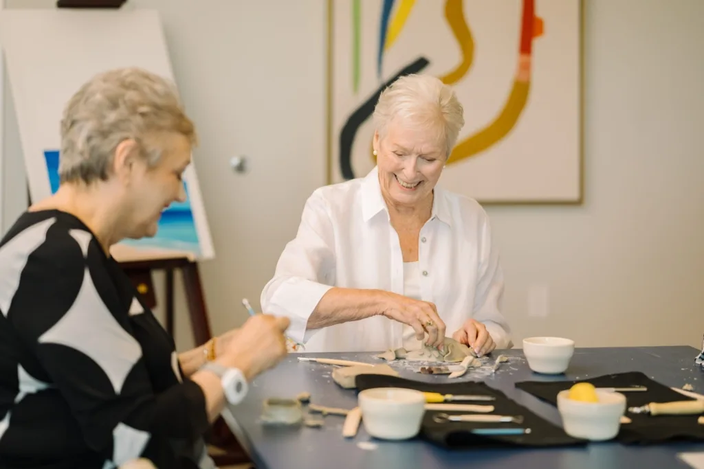 Two joyful residents engage in a creative pottery session, fostering community and connection.