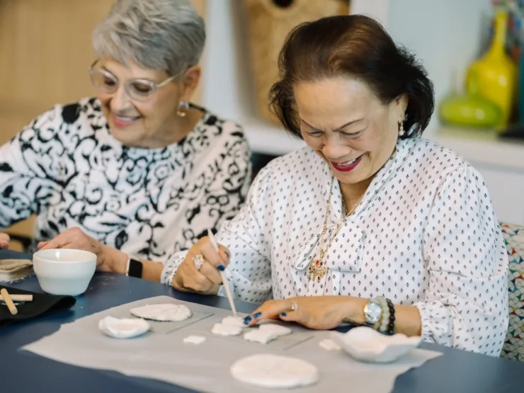 Two residents engage in a joyful art session, sharing smiles and creativity in a vibrant, welcoming space.