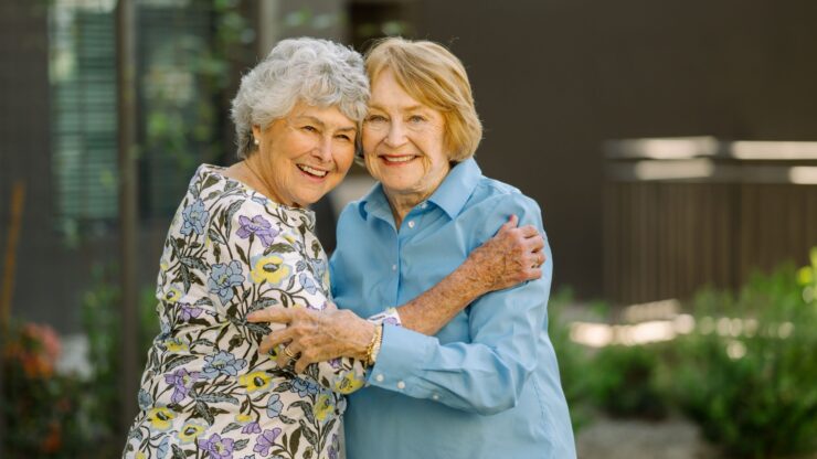 Two joyful women share a warm embrace in a vibrant garden, radiating friendship and community spirit.