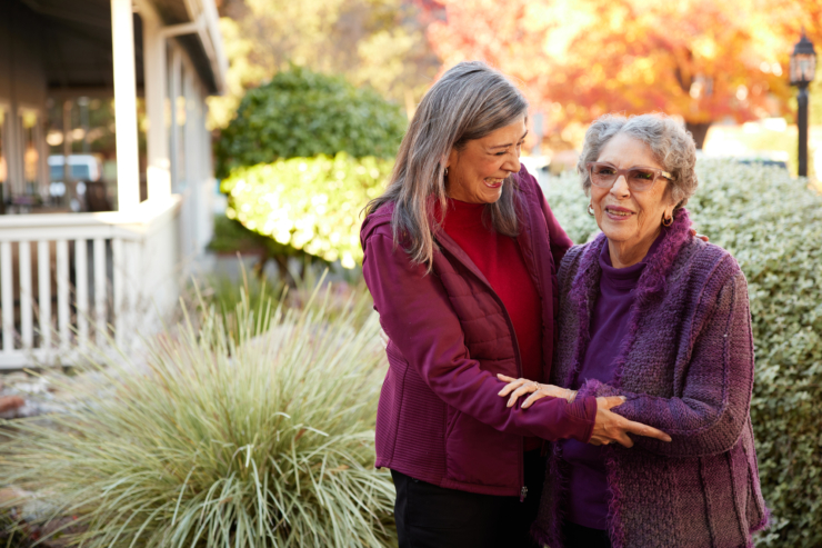 Two women share a joyful moment outdoors, surrounded by vibrant greenery and warm autumn colors, embodying community and connection.