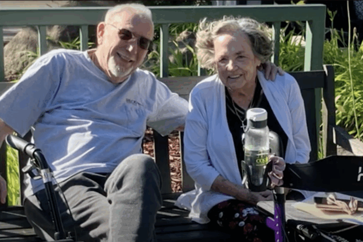Two smiling residents enjoy a sunny day together on a bench, embodying warmth and community spirit.