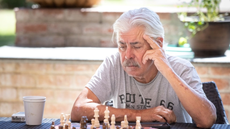 A thoughtful gentleman enjoys a game of chess outdoors, surrounded by a serene and welcoming atmosphere.