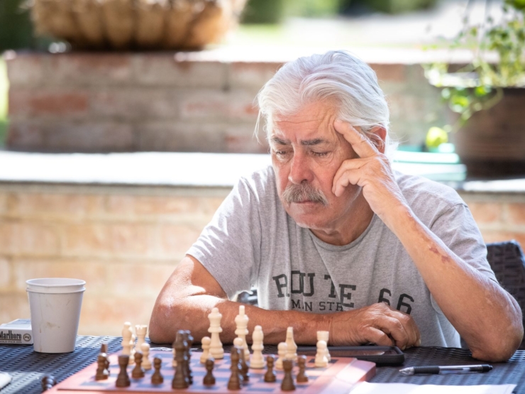 A thoughtful gentleman enjoys a game of chess outdoors, surrounded by a serene and welcoming atmosphere.
