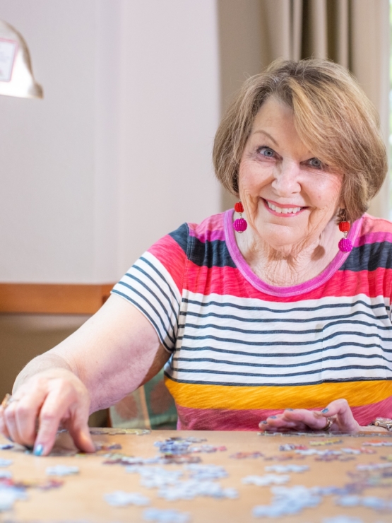 A cheerful resident enjoys a puzzle, surrounded by natural light and a warm, inviting atmosphere.