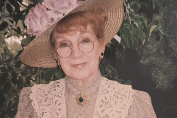 A smiling woman in a beautiful garden wears a stylish hat, exuding warmth and community spirit.