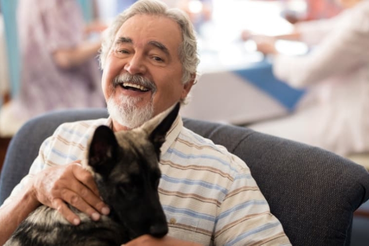 A smiling gentleman enjoys a warm moment with a dog, surrounded by a vibrant community atmosphere.