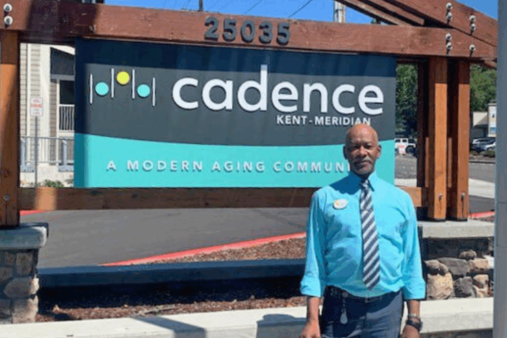A friendly staff member stands proudly outside Cadence Kent-Meridian, welcoming all to a vibrant community.