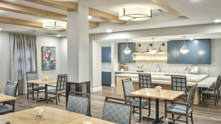 Bright, welcoming dining area with cozy tables, floral centerpieces, and a modern kitchen backdrop.