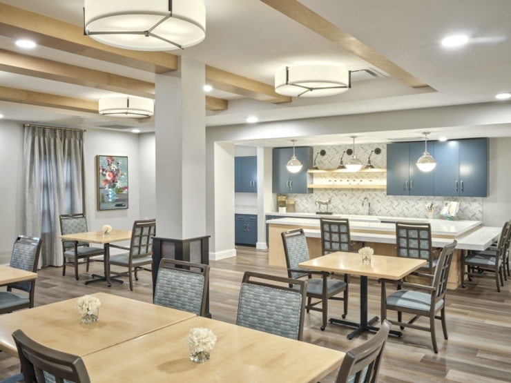 Bright, welcoming dining area with cozy tables, floral centerpieces, and a modern kitchen backdrop.
