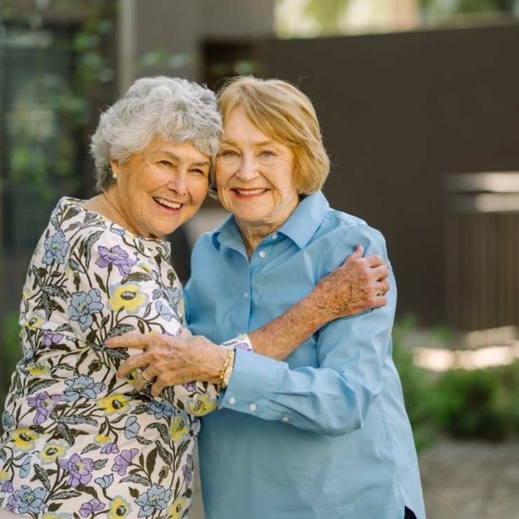 Two smiling women embrace warmly in a vibrant garden, radiating joy and community spirit.