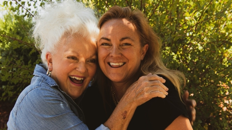 Two joyful women share a warm embrace, surrounded by lush greenery, radiating happiness and community.