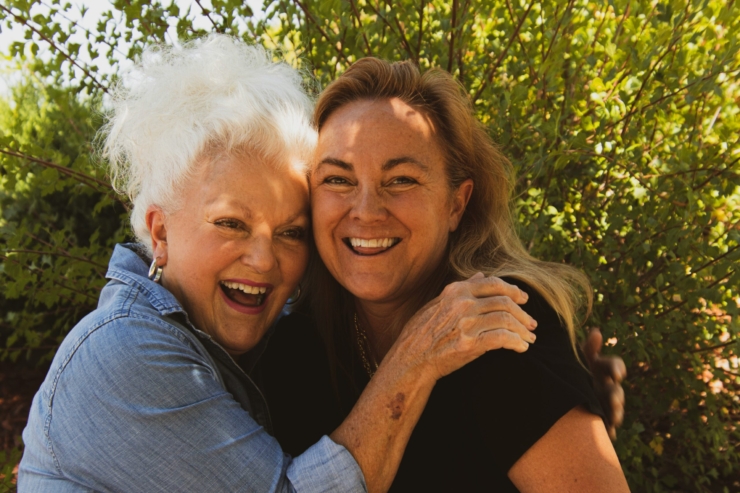 Two joyful women share a warm embrace, surrounded by lush greenery, radiating happiness and community.