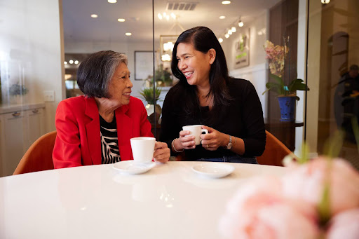 Two women share a joyful moment over coffee, surrounded by fresh blooms and a welcoming atmosphere.