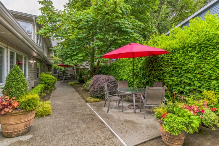 A serene garden pathway invites relaxation, featuring cozy seating under vibrant red umbrellas.
