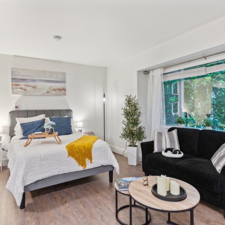 A bright, inviting room features a cozy bed and a comfortable sofa, enhanced by natural light and greenery.