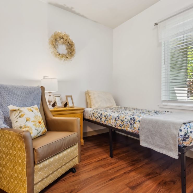 A cozy, well-lit room featuring a comfortable chair, inviting bed, and warm decor, perfect for relaxation.