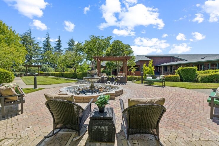 A serene outdoor space featuring comfortable seating, a gentle fountain, and lush greenery invites relaxation and community gatherings.