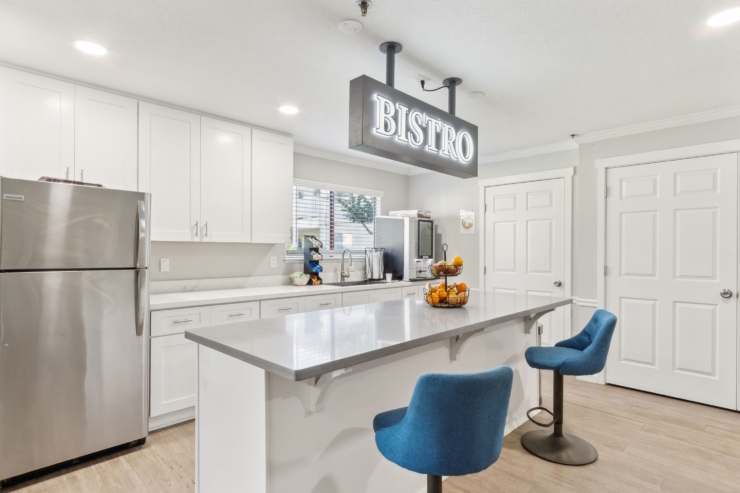 A modern bistro kitchen invites connection, featuring bright decor, fresh fruit, and cozy seating.