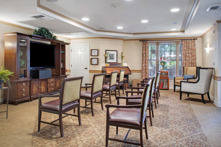 Well-lit activity room with arranged seating, a piano, and a large window overlooking greenery.