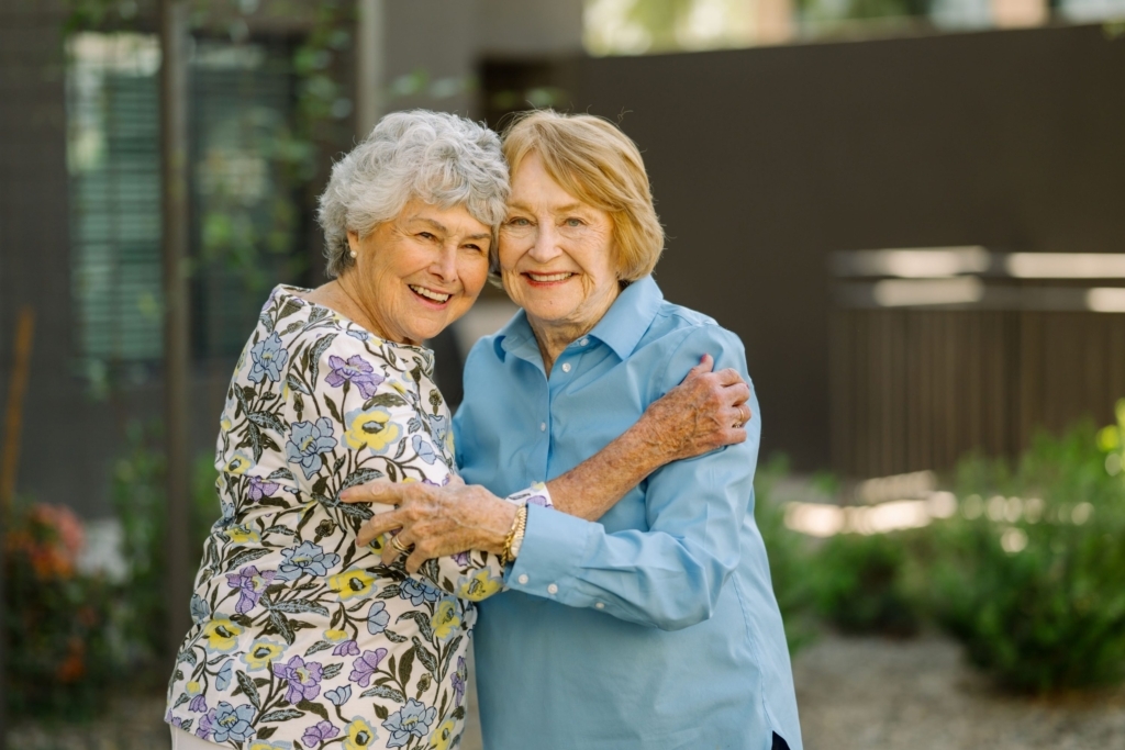 Two smiling women embrace warmly in a vibrant garden, radiating joy and friendship.