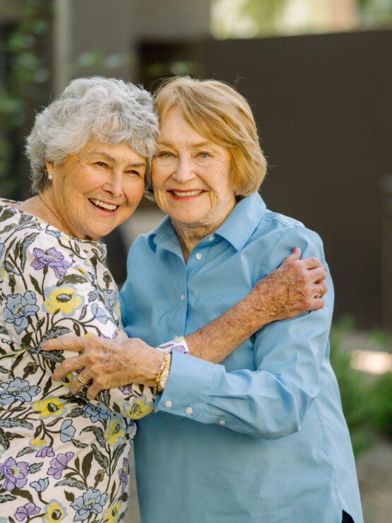 Two smiling women embrace warmly in a vibrant garden, radiating joy and friendship.