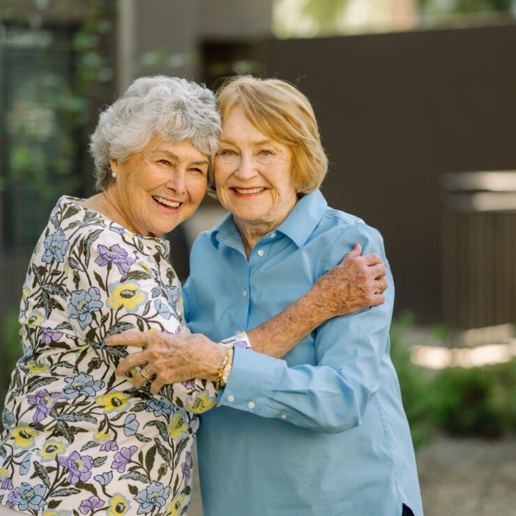 Two smiling women embrace warmly in a vibrant garden, radiating joy and friendship.