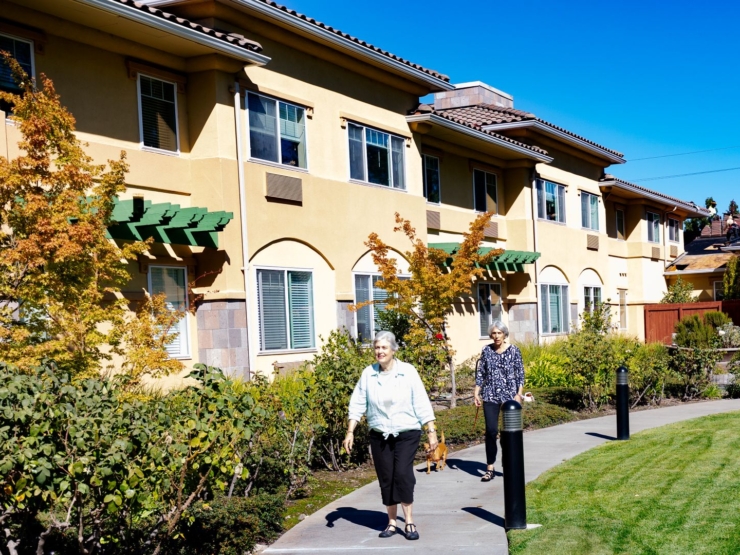 Two residents enjoy a sunny stroll along a landscaped path, surrounded by vibrant greenery.