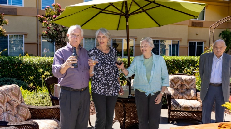 Residents enjoy a sunny gathering under an umbrella, sharing laughter and drinks in a welcoming atmosphere.