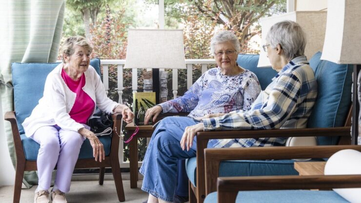 Three residents enjoy warm conversation on a sunny porch, fostering community and connection.