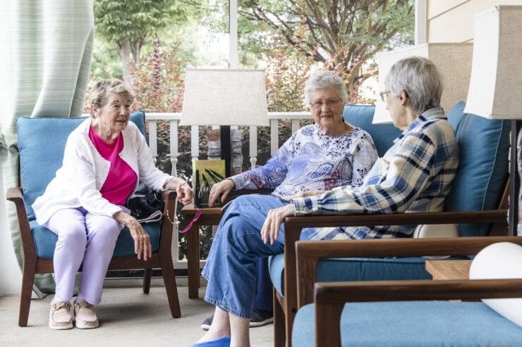 Three residents enjoy warm conversation on a sunny porch, fostering community and connection.