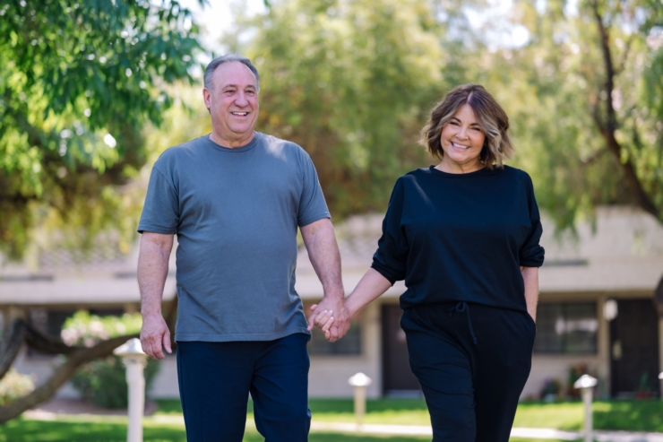 A joyful couple walks hand in hand through a lush, sunny garden, radiating warmth and companionship.