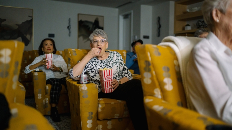 Seniors enjoy a movie night together, savoring popcorn in comfortable chairs, fostering community and joy.