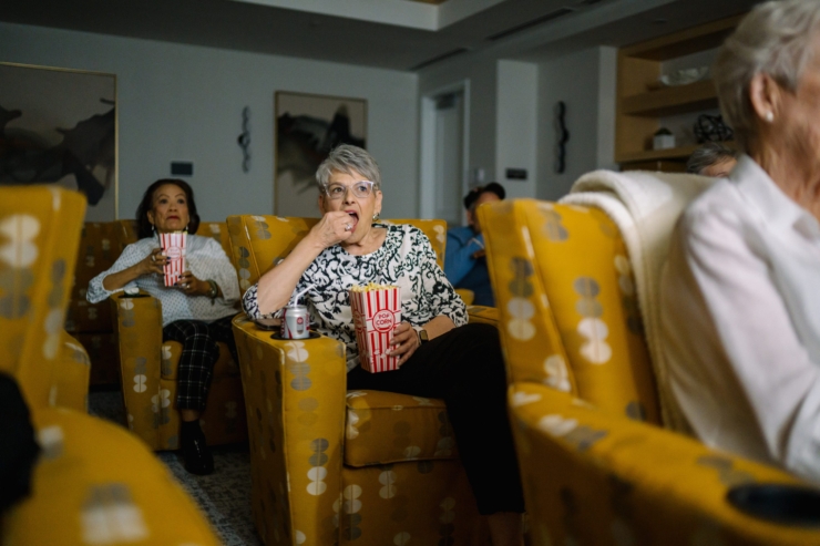 Seniors enjoy a movie night together, savoring popcorn in comfortable chairs, fostering community and joy.