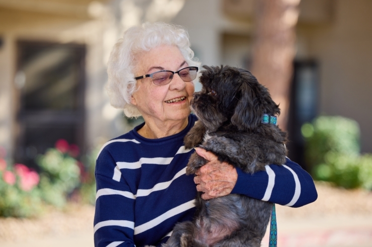 A joyful moment shared between a resident and her dog, surrounded by a vibrant garden.