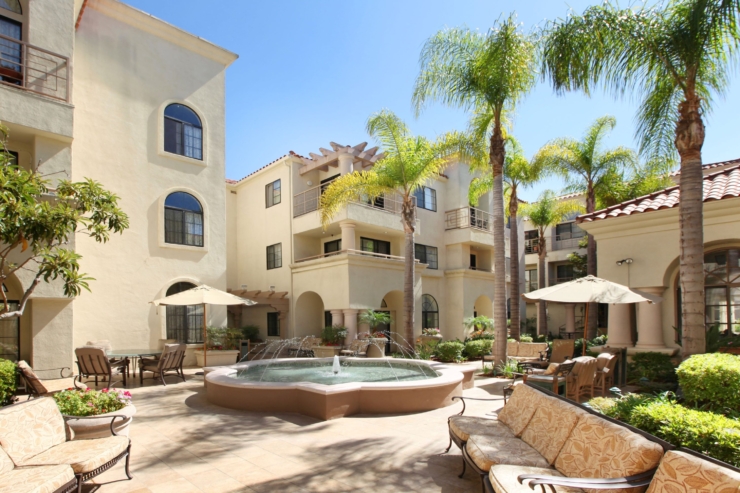 A serene courtyard with lush palms, inviting seating, and a tranquil fountain fosters community and warmth.