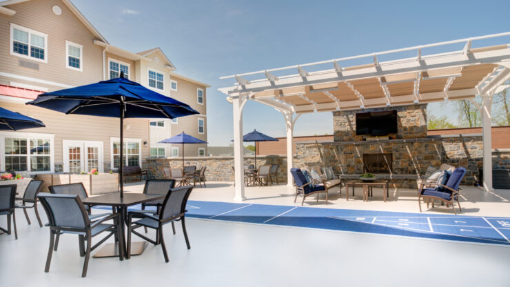 Outdoor seating with umbrellas and a shaded lounge area around a fireplace for community gathering.