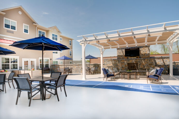 Outdoor seating with umbrellas and a shaded lounge area around a fireplace for community gathering.