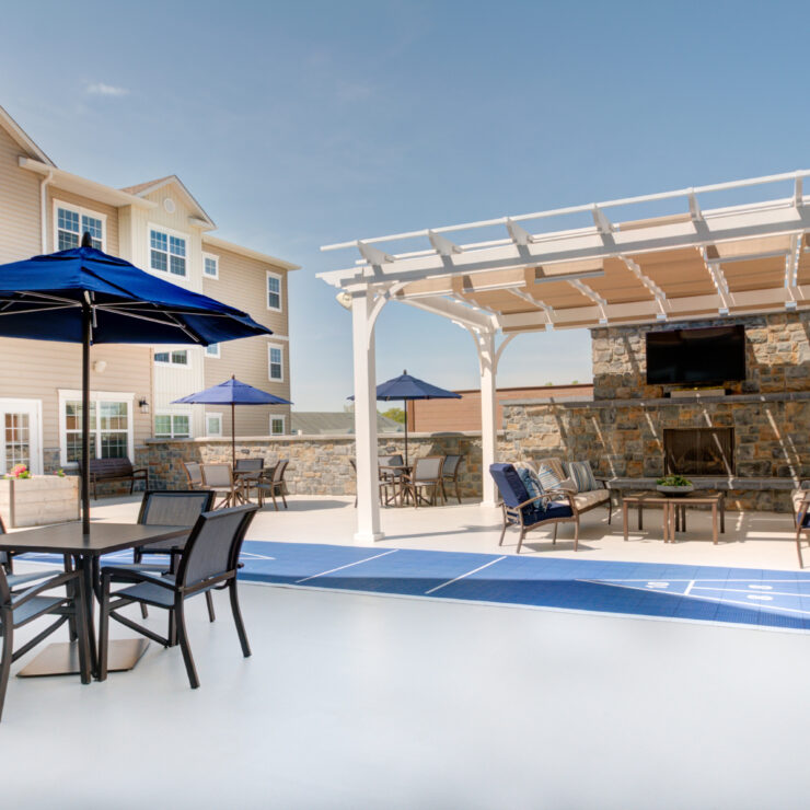 Outdoor seating with umbrellas and a shaded lounge area around a fireplace for community gathering.