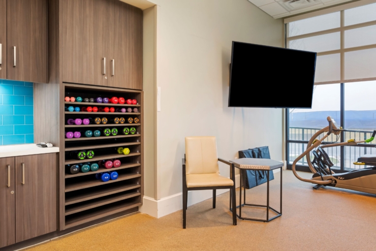 A bright and inviting fitness area, featuring colorful weights, cozy seating, and a view of nature.