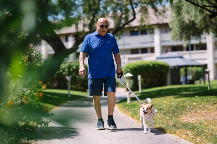 A resident enjoys a pleasant stroll with a dog, surrounded by lush greenery and a welcoming community.