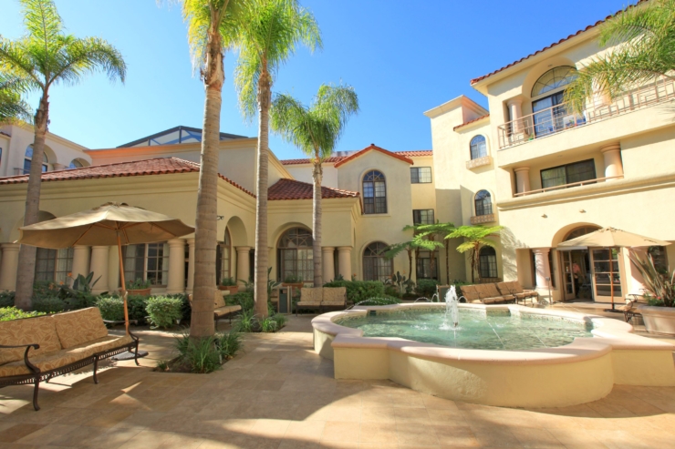 A serene courtyard features lush palms and a gentle fountain, inviting relaxation and community.