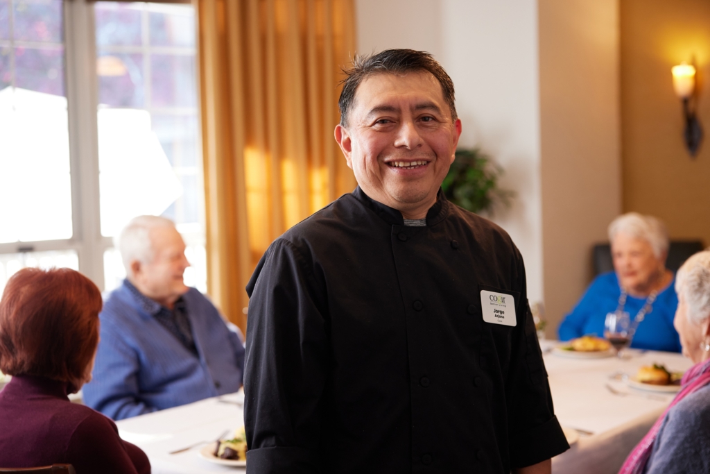A cheerful chef engages warmly with residents, creating a welcoming and vibrant dining atmosphere.