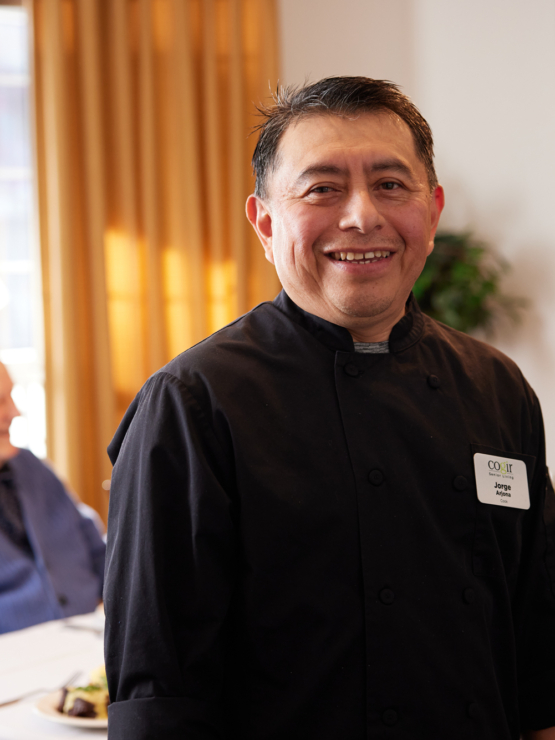 A cheerful chef engages warmly with residents, creating a welcoming and vibrant dining atmosphere.