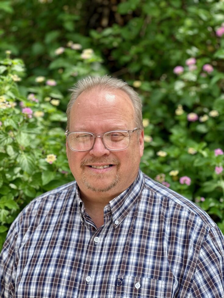 A friendly resident smiles warmly against a backdrop of vibrant greenery, embodying community and warmth.