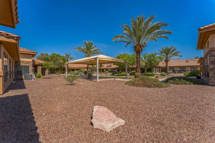 A welcoming outdoor space featuring shaded seating, surrounded by lush greenery and vibrant palm trees.