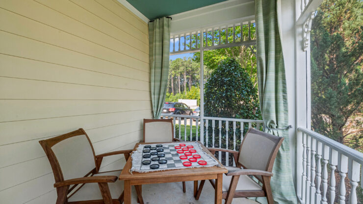 A welcoming porch invites relaxation, featuring a checkerboard table and comfortable seating for friendly gatherings.