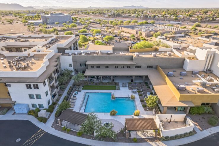 A vibrant community space with a serene pool, surrounded by lush greenery and welcoming architecture.