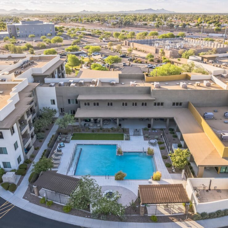 A vibrant community space with a serene pool, surrounded by lush greenery and welcoming architecture.