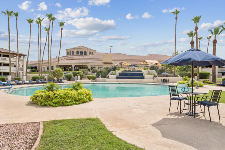 A serene poolside setting invites relaxation and community, surrounded by lush greenery and sunny skies.